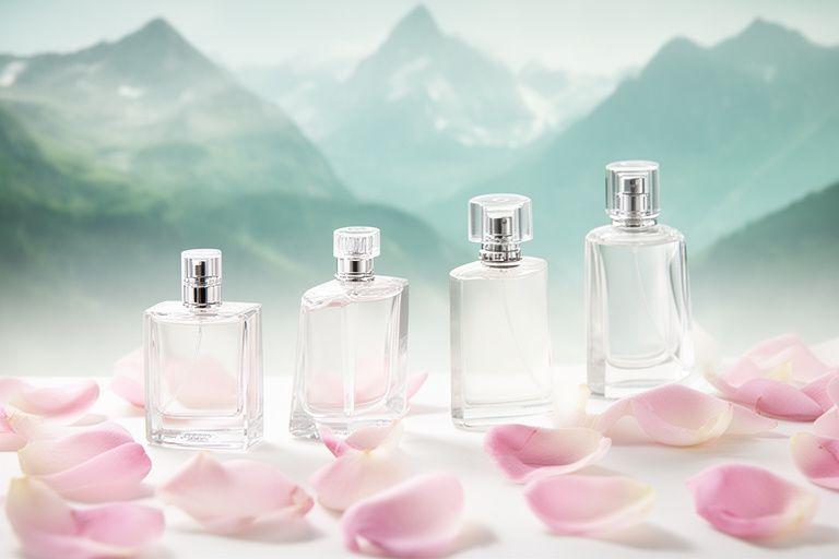 Hell beleuchtete Parfümflakons mit Rosenblättern und alpiner Landschaft als weiche Kulisse